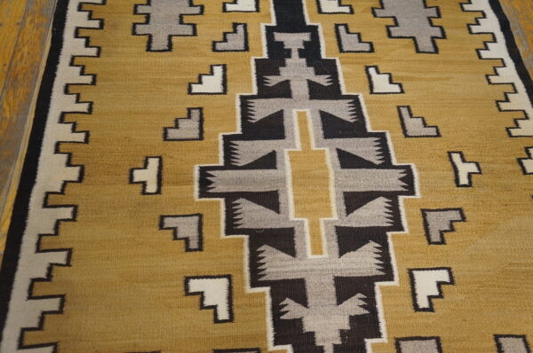 Geometric flatweave rug in gold, black, gray, and cream sits on light wood flooring.