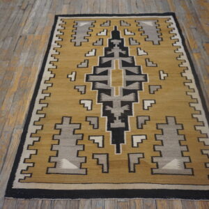 A flatweave rug with a geometric pattern in mustard, black, gray, and cream rests on distressed wood planks.