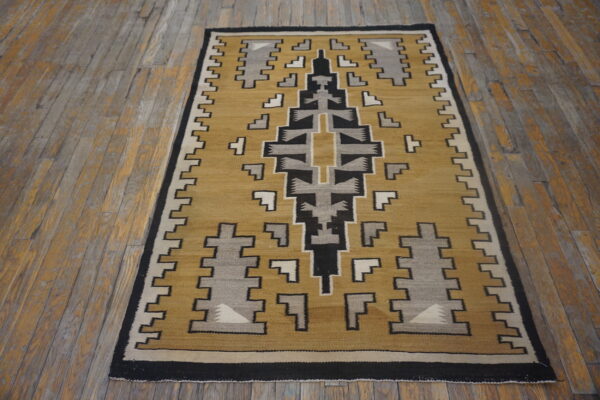 A flatweave rug with a geometric pattern in mustard, black, gray, and cream rests on distressed wood planks.