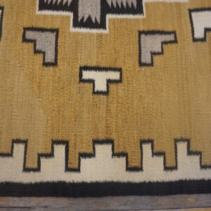 Geometric flatweave rug in tan, white, gray, and black resting on dark distressed wood.