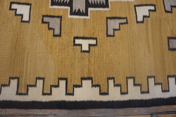 Geometric flatweave rug in tan, white, gray, and black resting on dark distressed wood.