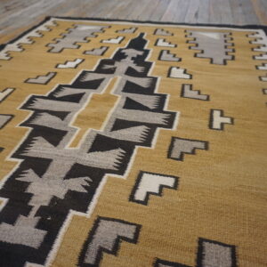 Gold, black, gray, and cream geometric flat weave rug displayed on rustic wooden plank flooring.