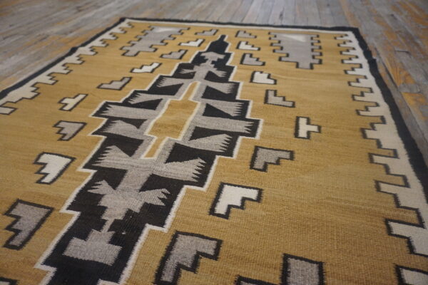 Gold, black, gray, and cream geometric flat weave rug displayed on rustic wooden plank flooring.