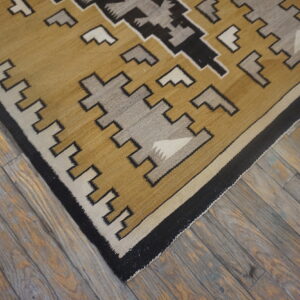 Tan, gray, black, and cream flatweave rug with a stepped geometric design lies on rustic wooden floorboards.
