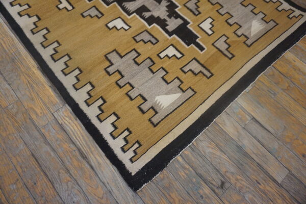Tan, gray, black, and cream flatweave rug with a stepped geometric design lies on rustic wooden floorboards.