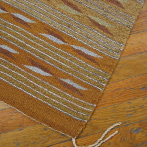 Earth-toned rug featuring stripes and geometric shapes in orange, olive, and gray on distressed wood flooring.