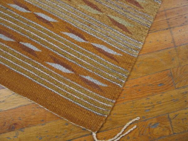 Earth-toned rug featuring stripes and geometric shapes in orange, olive, and gray on distressed wood flooring.