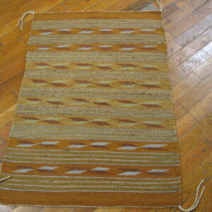 Gold and brown flatweave rug featuring geometric stripes rests on a diagonal plank wood floor.