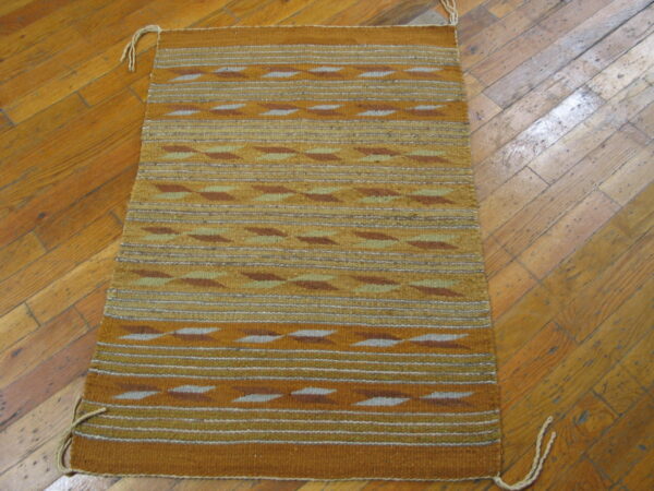 Gold and brown flatweave rug featuring geometric stripes rests on a diagonal plank wood floor.