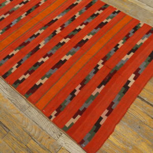Bright orange flatweave rug with multicolored geometric stripes lying diagonally on rustic wood flooring.