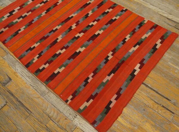 Bright orange flatweave rug with multicolored geometric stripes lying diagonally on rustic wood flooring.