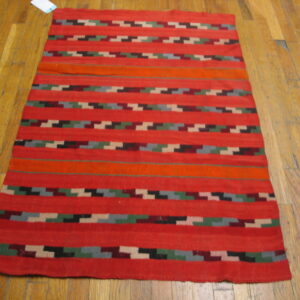 Red flatweave rug with bold horizontal stripes and multicolor zigzag designs on a wood floor.