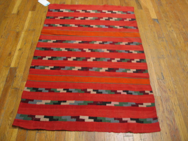 Red flatweave rug with bold horizontal stripes and multicolor zigzag designs on a wood floor.