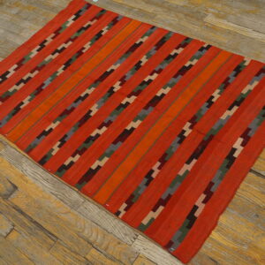 Red flatweave rug with dark, multi-colored stepped stripe patterns lying diagonally on distressed wood floor.