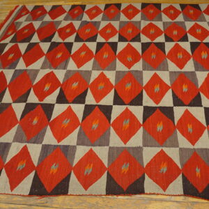 Red, dark brown, and gray geometric flatweave rug with small colorful accents rests on a worn wood floor.