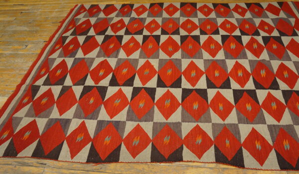 Red, dark brown, and gray geometric flatweave rug with small colorful accents rests on a worn wood floor.