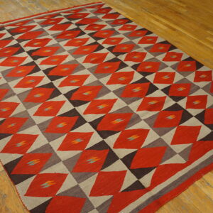 Red, taupe, and dark brown flatweave rug featuring a repeating geometric diamond pattern on wood flooring.