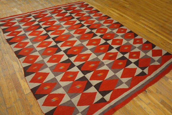 Red, taupe, and dark brown flatweave rug featuring a repeating geometric diamond pattern on wood flooring.