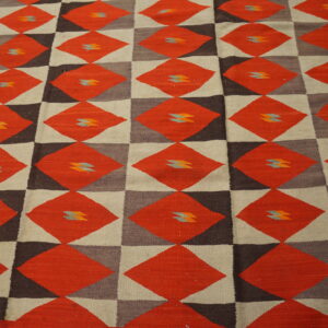 Red and brown geometric diamond flatweave rug with small blue motifs rests on light wood flooring.