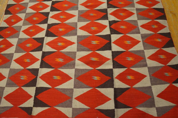 Red and brown geometric diamond flatweave rug with small blue motifs rests on light wood flooring.