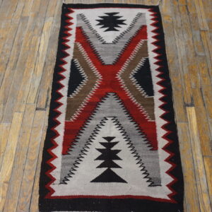 Geometric flat woven runner in black, red, white, gray, and brown rests on distressed wood flooring.