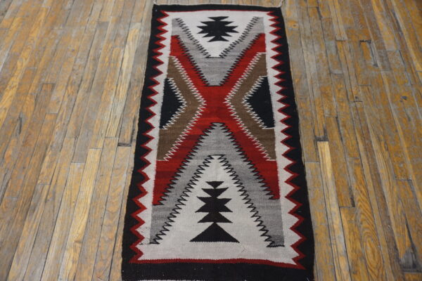 Geometric flat woven runner in black, red, white, gray, and brown rests on distressed wood flooring.