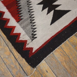 Black, red, gray, and cream geometric flatweave rug corner rests on rustic wood floorboards.