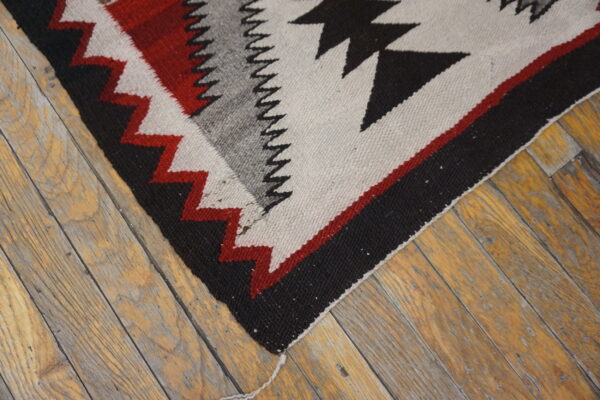 Black, red, gray, and cream geometric flatweave rug corner rests on rustic wood floorboards.