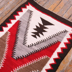 Flatwoven rug featuring red, cream, brown, gray, and black geometric patterns on distressed wood planks.