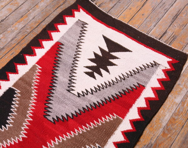 Flatwoven rug featuring red, cream, brown, gray, and black geometric patterns on distressed wood planks.