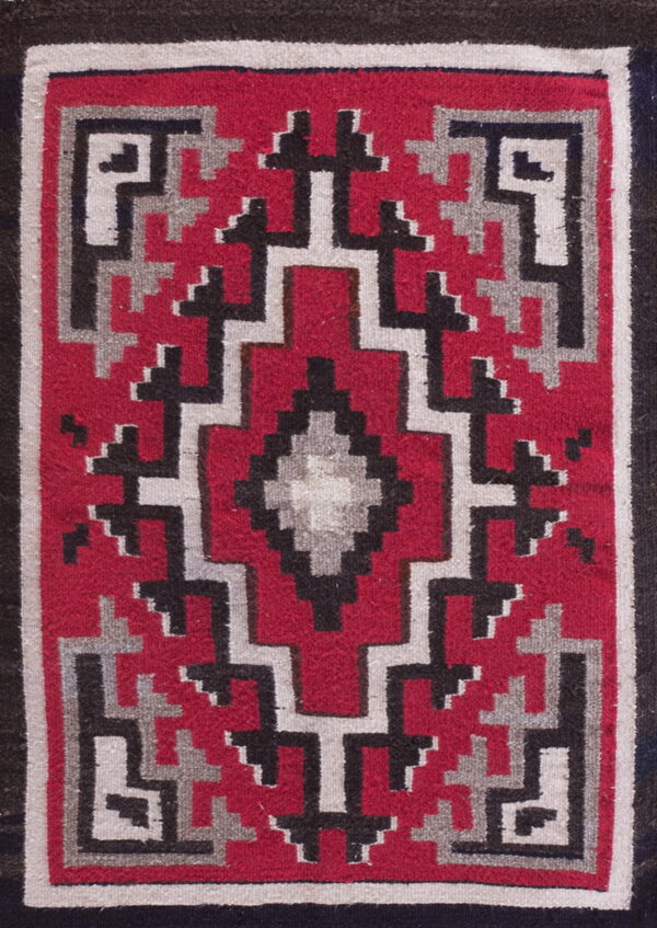 Flat-weave rug with a central diamond motif surrounded by red, black, and gray geometric borders.