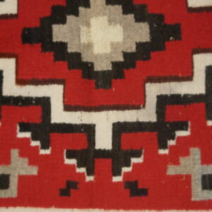 Red rug detail showing a stepped geometric pattern in black, white, and gray over wood floor.