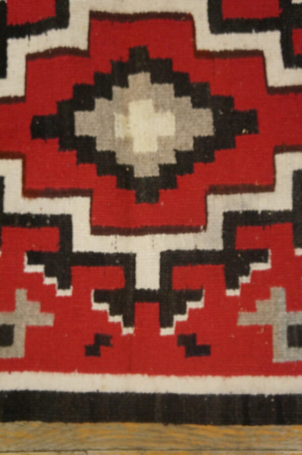 Red rug detail showing a stepped geometric pattern in black, white, and gray over wood floor.