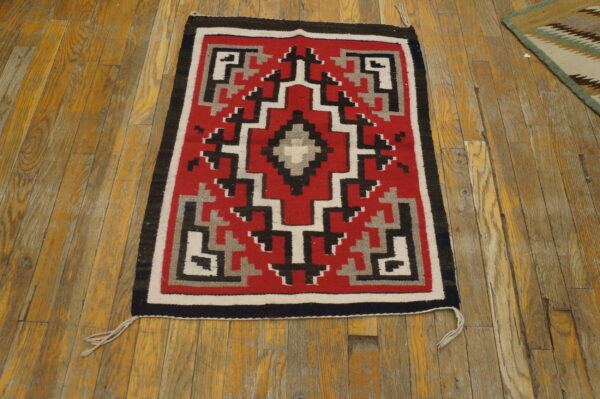 Red, black, white, and gray flat-weave geometric rug placed on worn plank hardwood flooring.
