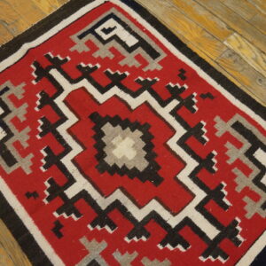 Red, black, white, and gray geometric rug displayed on rustic wooden plank floors.