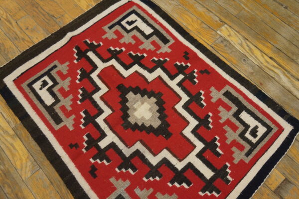 Red, black, white, and gray geometric rug displayed on rustic wooden plank floors.