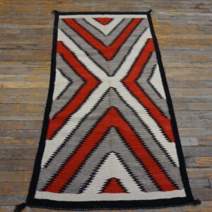Red, gray, black, and white serrated zigzag runner rug on distressed plank wood flooring.