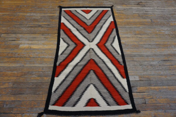 Red, gray, black, and white serrated zigzag runner rug on distressed plank wood flooring.