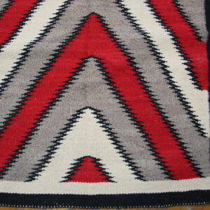 Flatweave rug with serrated red, gray, and cream zigzags bordered in black, resting on wood planks.