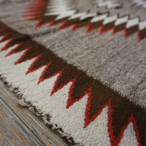 Rustic low-pile rug featuring large zigzag designs in brown, cream, and red-orange on distressed wood planks.