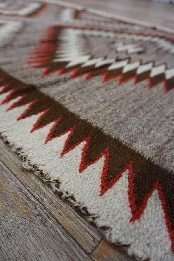 Rustic low-pile rug featuring large zigzag designs in brown, cream, and red-orange on distressed wood planks.