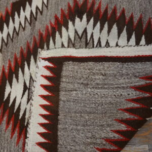 Geometric flatweave rug featuring gray, dark brown, white, and red sawtooth designs on a wood floor.