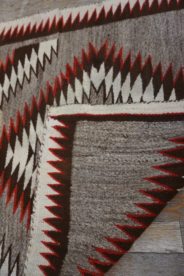 Geometric flatweave rug featuring gray, dark brown, white, and red sawtooth designs on a wood floor.