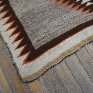 Flatwoven gray rug with brown, cream, and orange geometric border lying on distressed wood flooring.