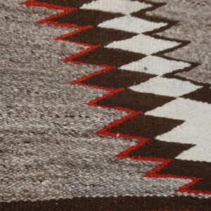 Close-up of a flatweave rug featuring mottled gray, dark brown, off-white, and red zigzag geometric patterns.