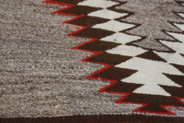 Close-up of a flatweave rug featuring mottled gray, dark brown, off-white, and red zigzag geometric patterns.