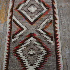 Flatweave rug in grey, white, brown, and rust tones features serrated diamond patterns on distressed wood planks.