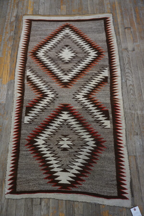 Flatweave rug in grey, white, brown, and rust tones features serrated diamond patterns on distressed wood planks.