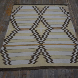 Pale, tan, and brown flatwoven rug featuring large diamond and zigzag geometric patterns on worn wood planks.
