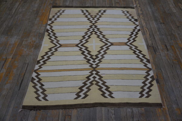 Pale, tan, and brown flatwoven rug featuring large diamond and zigzag geometric patterns on worn wood planks.